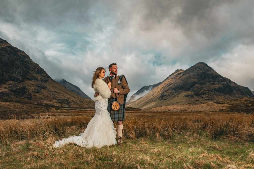 Bride in wedding dress and groom wearing kilt, outside in the Scottish Highlands.