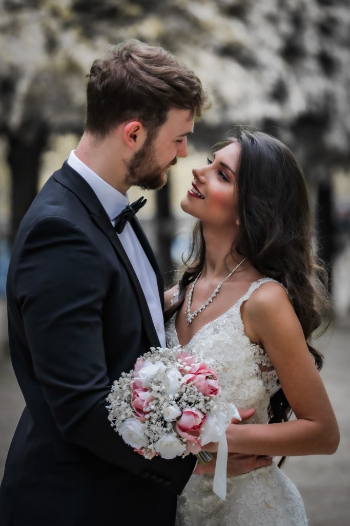 Bride, holding bouquet, and groom embracing and looking into each other's eyes.