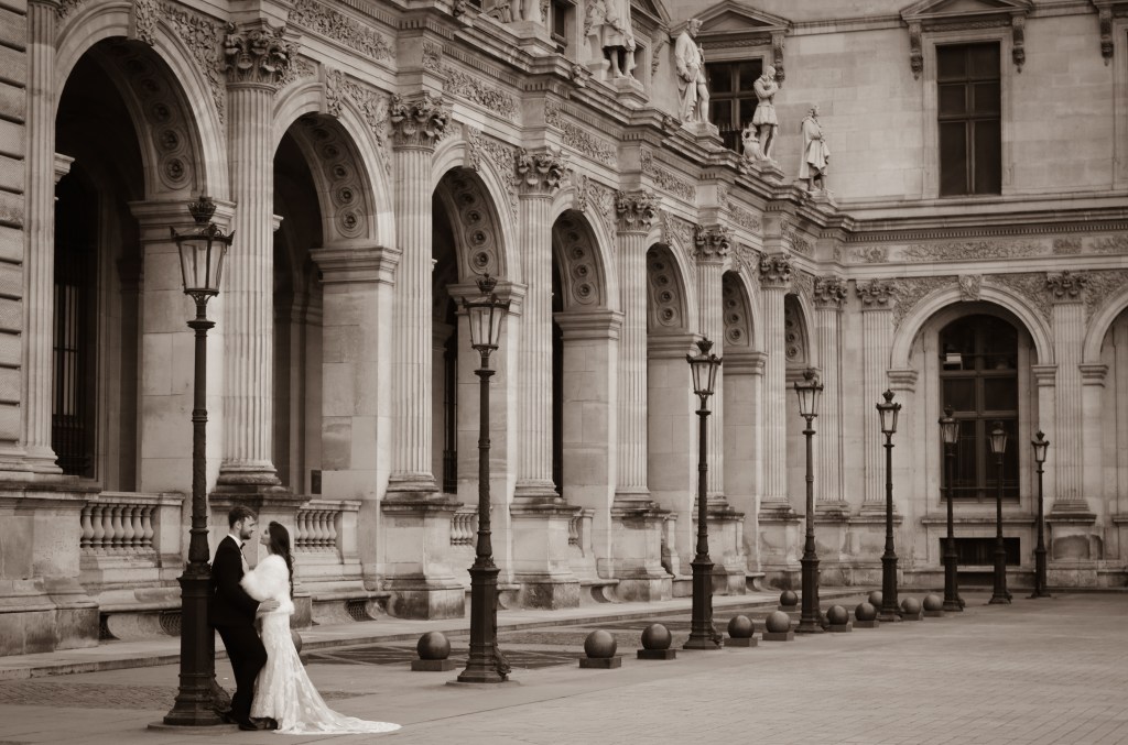 Bride and groom by ornate lamppost and arches.