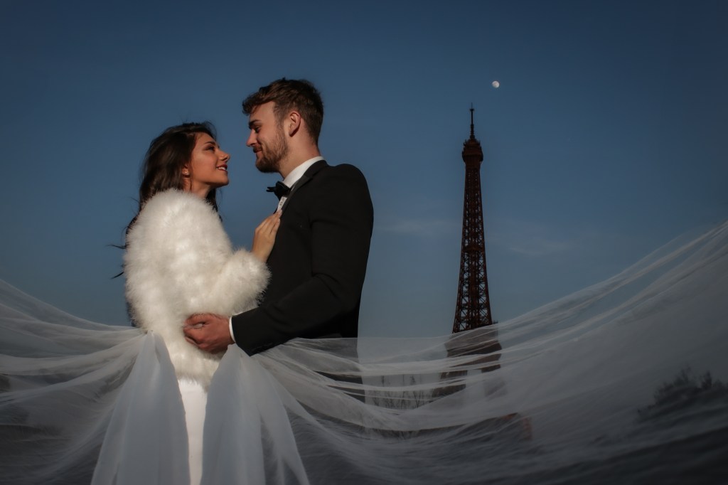 Bride and groom by the Eiffel Tower at night.